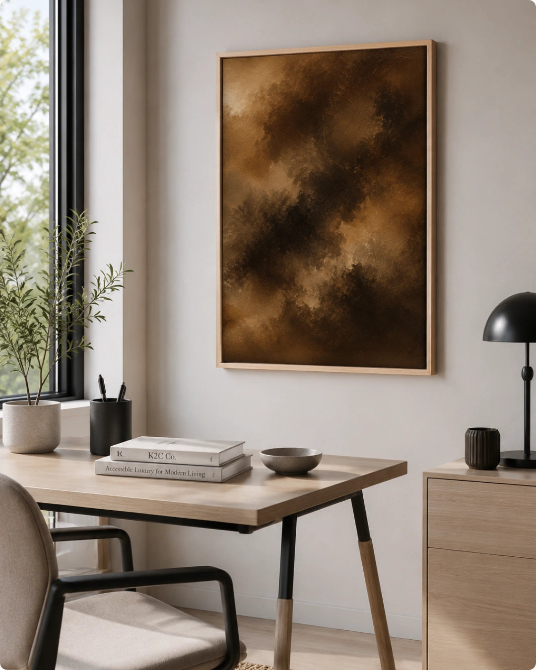 A framed abstract art print featuring a textured blend of dark brown, bronze, and gold tones, hanging on a light gray wall in a modern, sunlit home office setting.