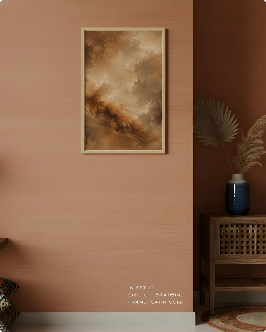 A framed abstract landscape art print in warm earthy tones of brown, beige, and gold, displayed on a textured terracotta wall in a styled interior setting.