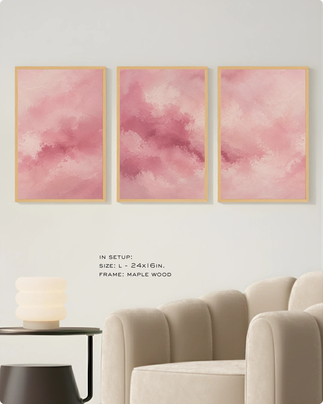 Three vertical pink watercolor art prints with light wood maple frames are displayed on a light gray wall above a beige armchair and a small side table.