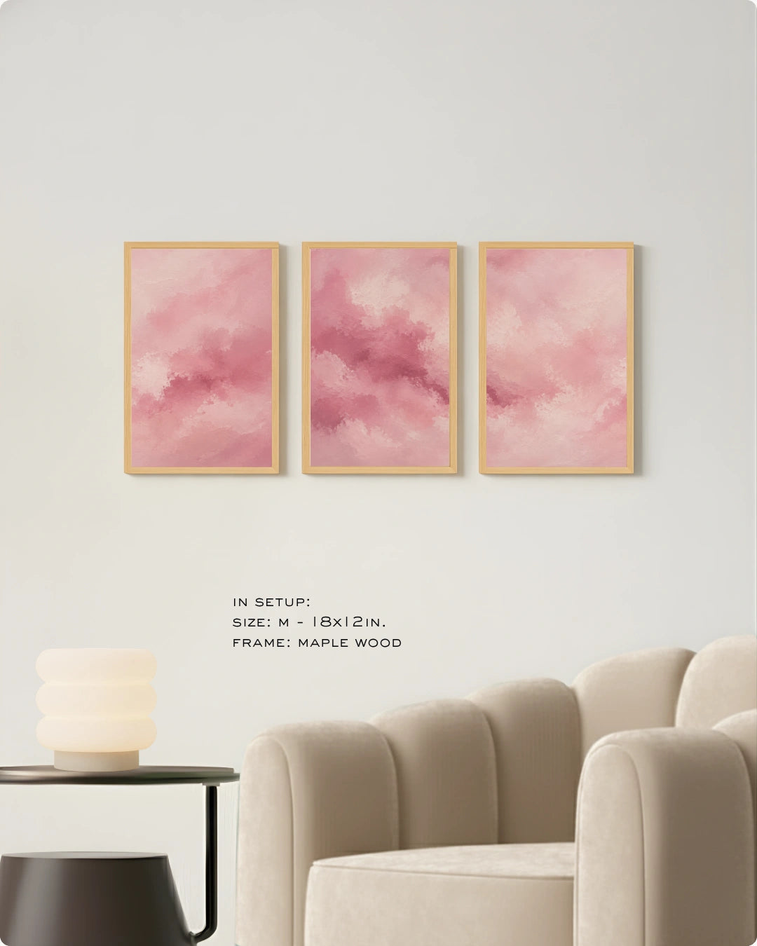 Three vertical framed wall art prints with pink watercolor clouds hang on a light gray wall above a beige armchair and side table. Text below reads: 'IN SETUP: SIZE: M - 18x12 IN.