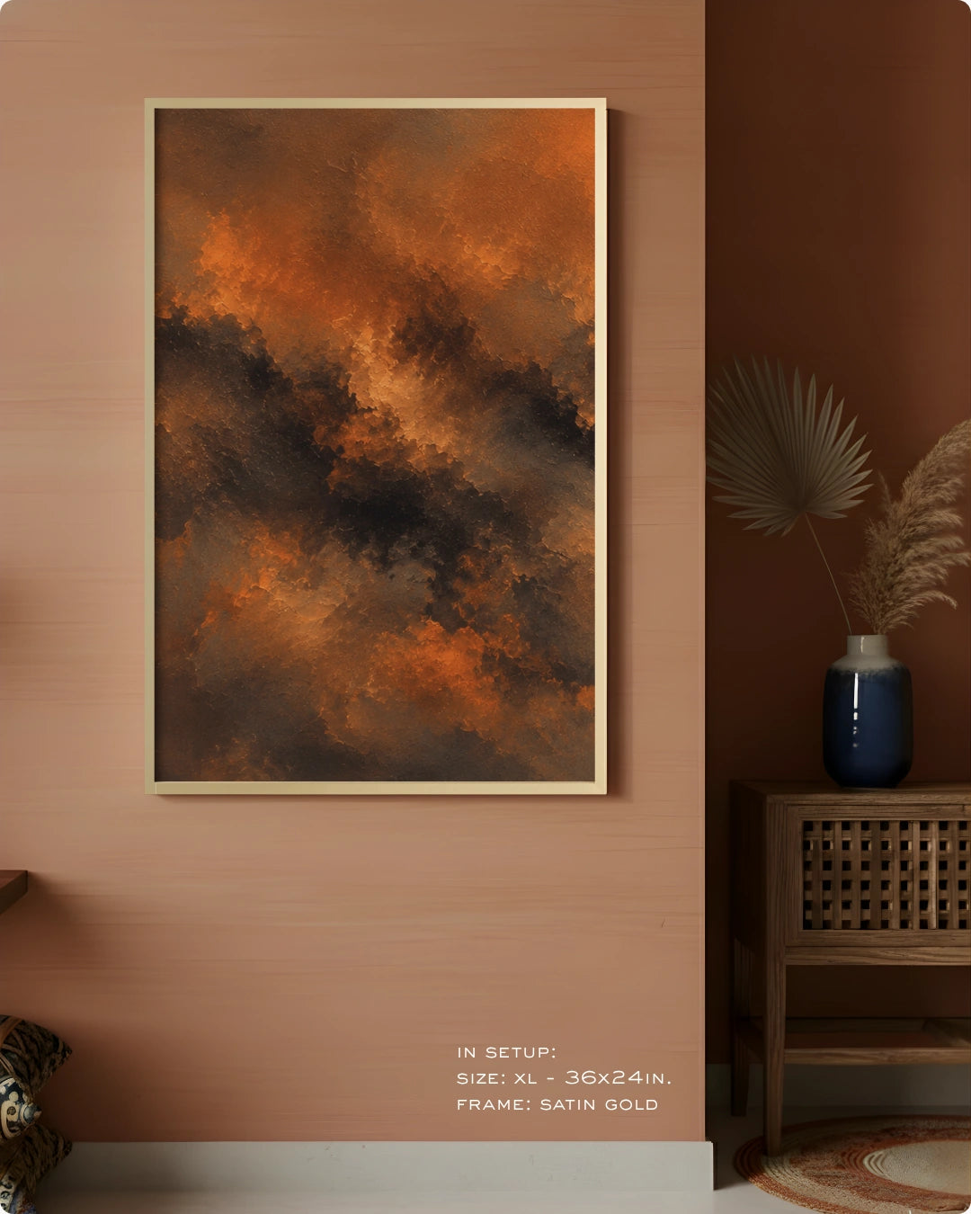 A framed abstract wall art print hangs on a warm peach wall in a styled interior. The artwork features swirling orange, brown, and dark charcoal tones, with a thin satin gold frame.