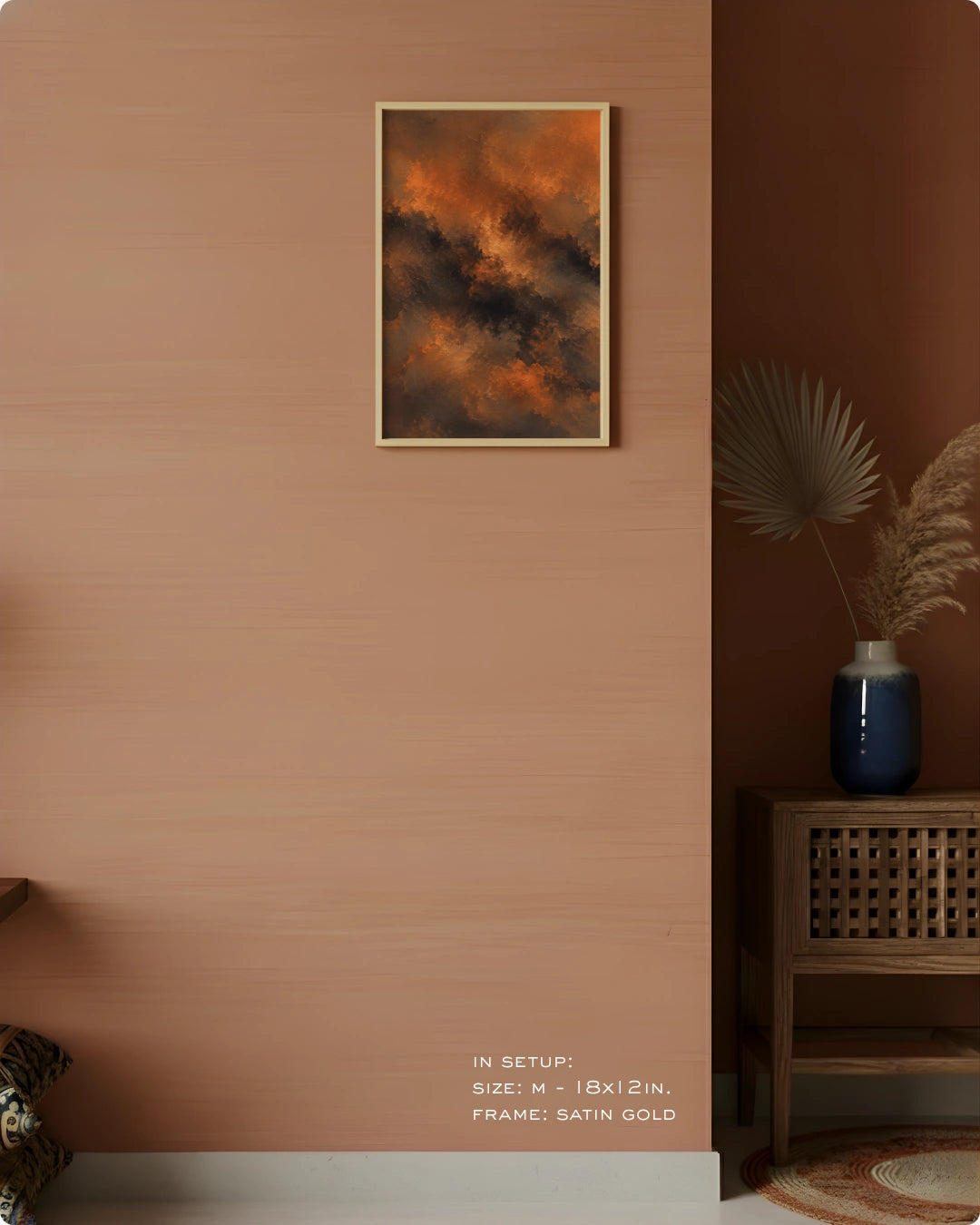 A framed abstract art print featuring fiery orange, brown, and black clouds, hung on a textured terracotta wall in a styled interior setting with a wooden side table and vase.