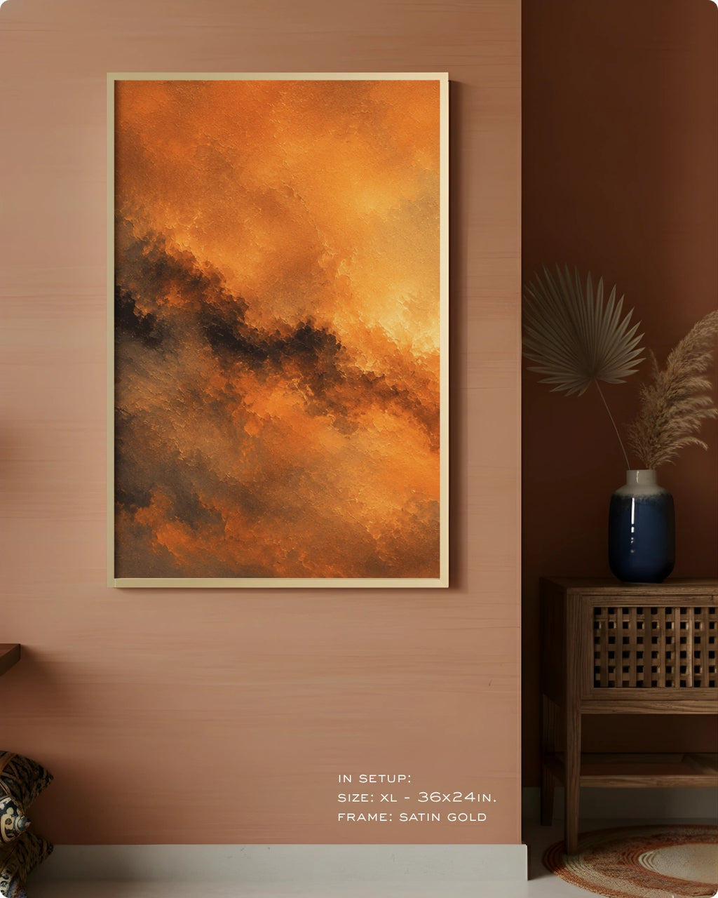 An abstract landscape art print featuring vibrant orange and brown clouds with dark gray accents, displayed in a gold frame on a warm terracotta wall in a styled room setting.