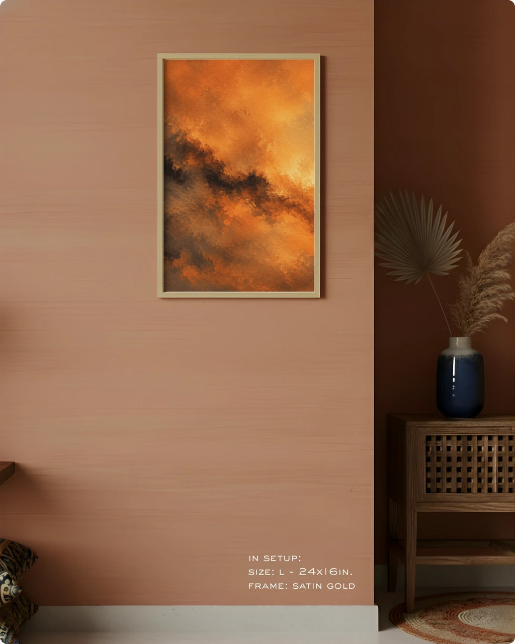 A framed abstract wall art print hangs on a warm peach-pink wall in a styled interior. The artwork shows swirling orange, gold, and dark brown cloud-like forms.