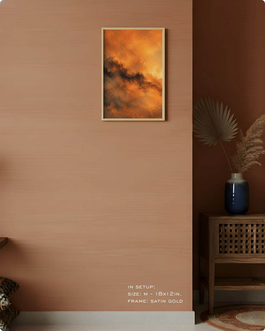 A framed abstract art print featuring vibrant orange and brown clouds hangs on a warm terracotta-colored wall in a styled interior setting with a wooden side table, blue vase, and dried palm leaves.