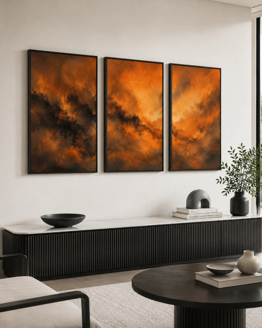 A three-panel framed wall art set with dramatic orange and brown abstract storm-like imagery, displayed above a black ribbed console in a modern living room.
