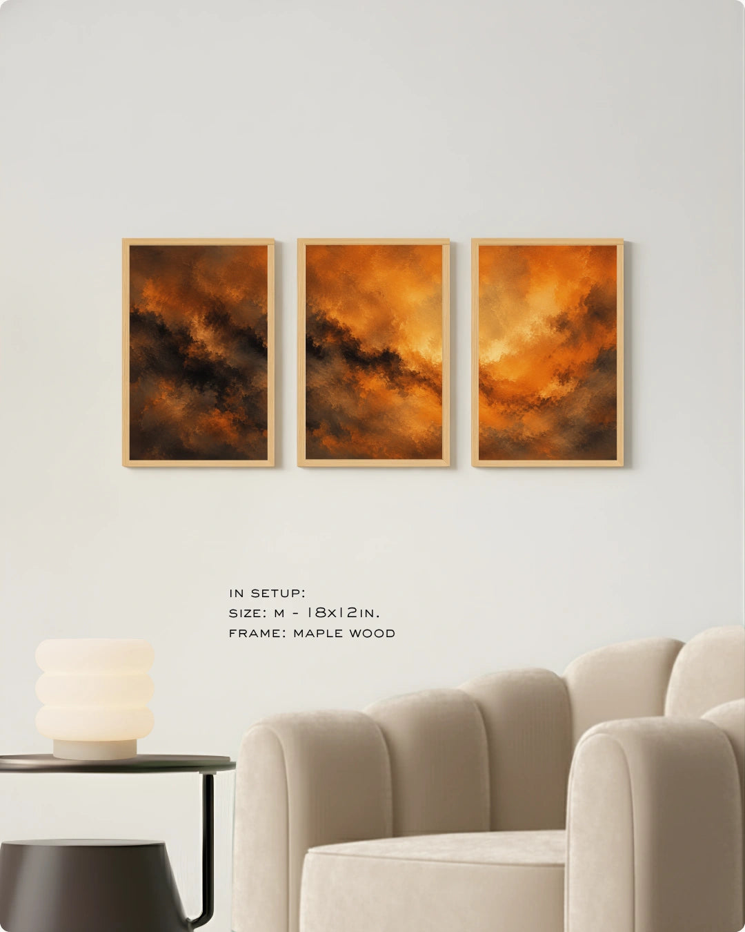 Three framed abstract wall art prints with fiery orange, brown, and black cloud-like imagery, displayed on a light gray wall above a cream sofa and side table. Text below reads: 'IN SETUP: SIZE: M - 18x12 IN.