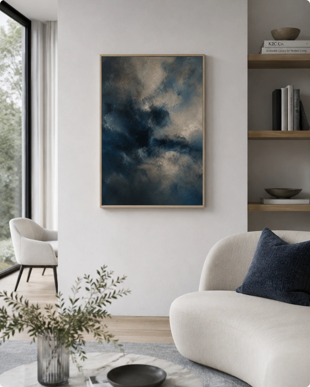 A framed abstract art print depicting a dramatic stormy sky in deep blue, gray, and white tones, displayed on a light gray wall in a modern living room setting.