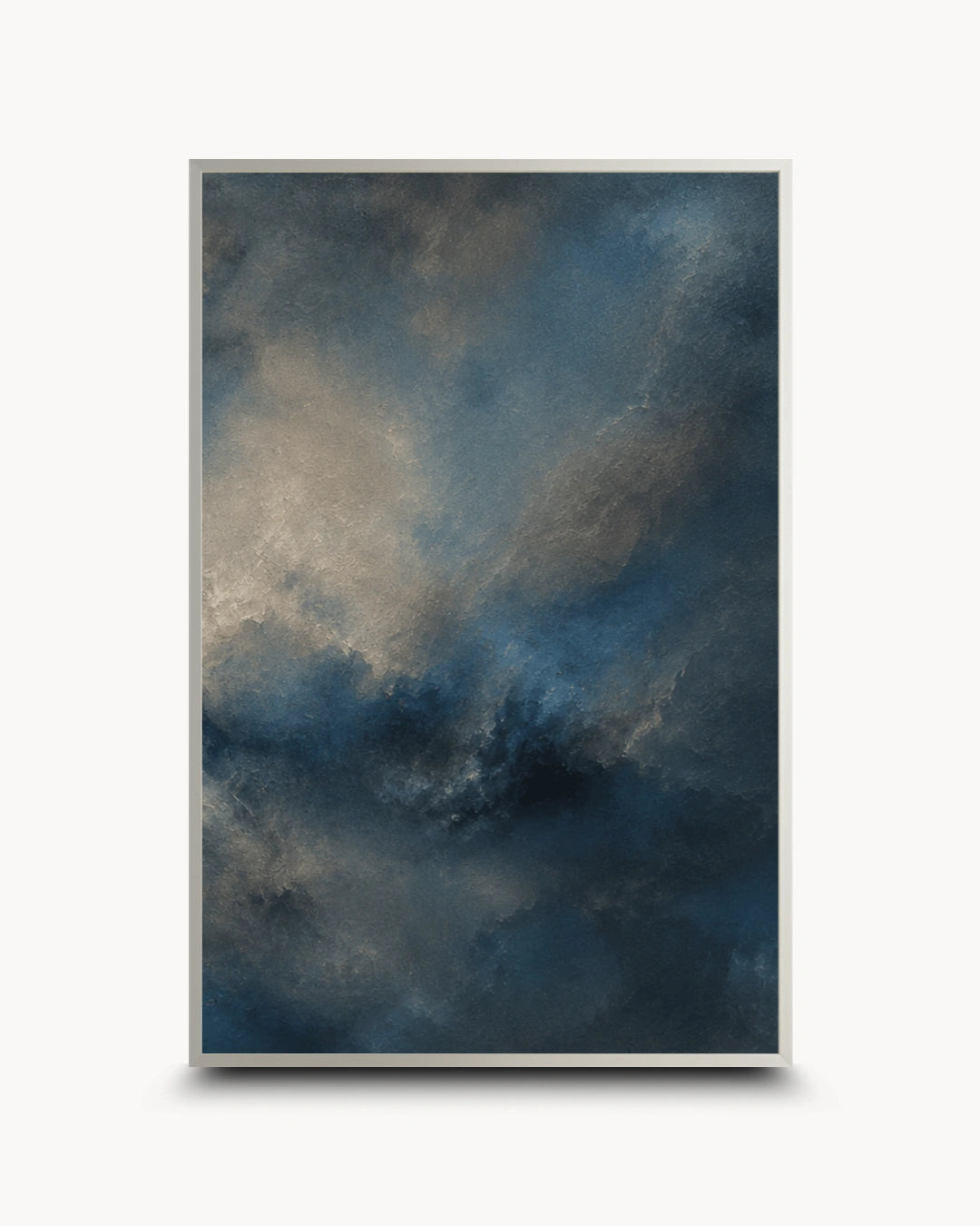 A framed abstract art print featuring a textured, painterly sky-like composition in deep blue, charcoal gray, and warm beige tones, enclosed in a thin gold frame against a light gray background.