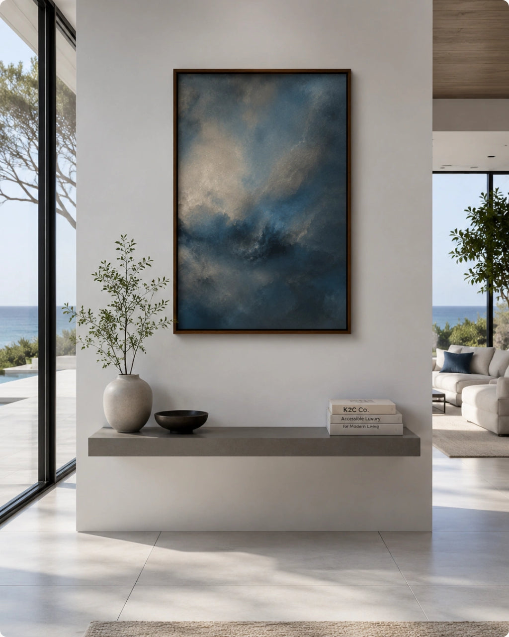 A framed vertical canvas print featuring a dramatic blue and gray cloudy sky, displayed on a white wall above a modern concrete console table in a bright, contemporary living space.
