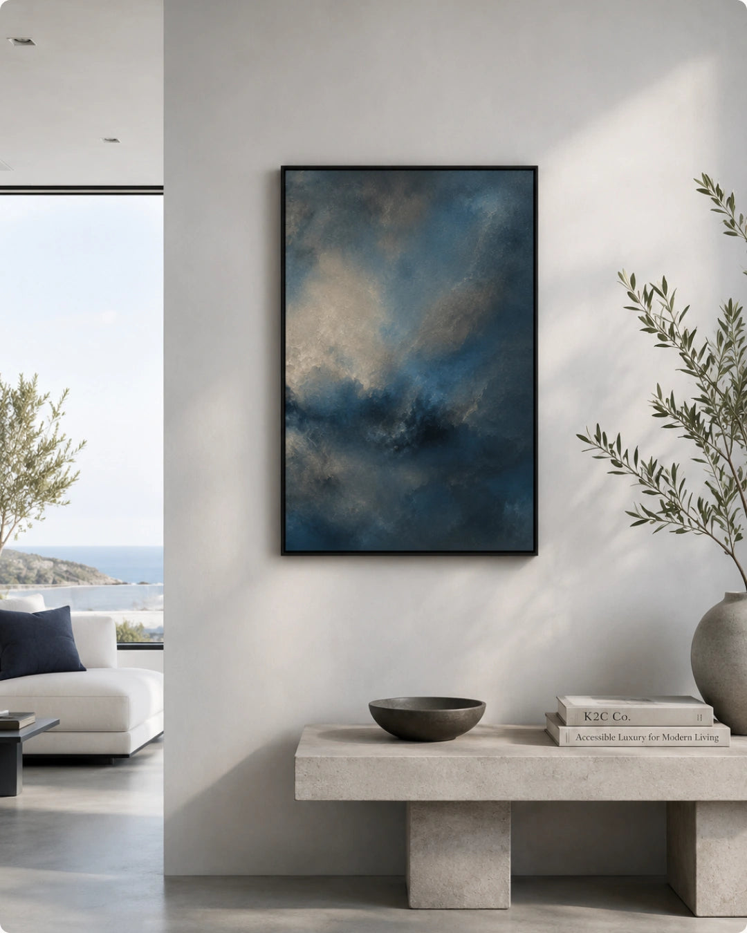 A framed abstract canvas print with swirling dark blue, gray, and beige tones hangs on a light gray wall in a modern living room setting.