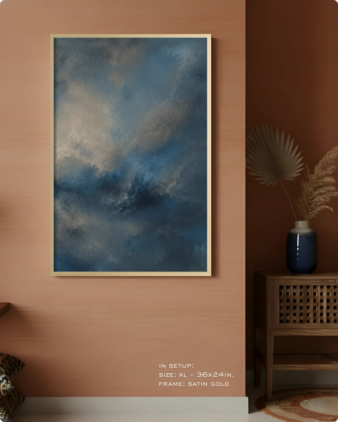 A framed wall art print featuring a dramatic blue and gray cloudy sky, displayed in a staged interior setting with a terracotta wall, wooden side table, and decorative vase.