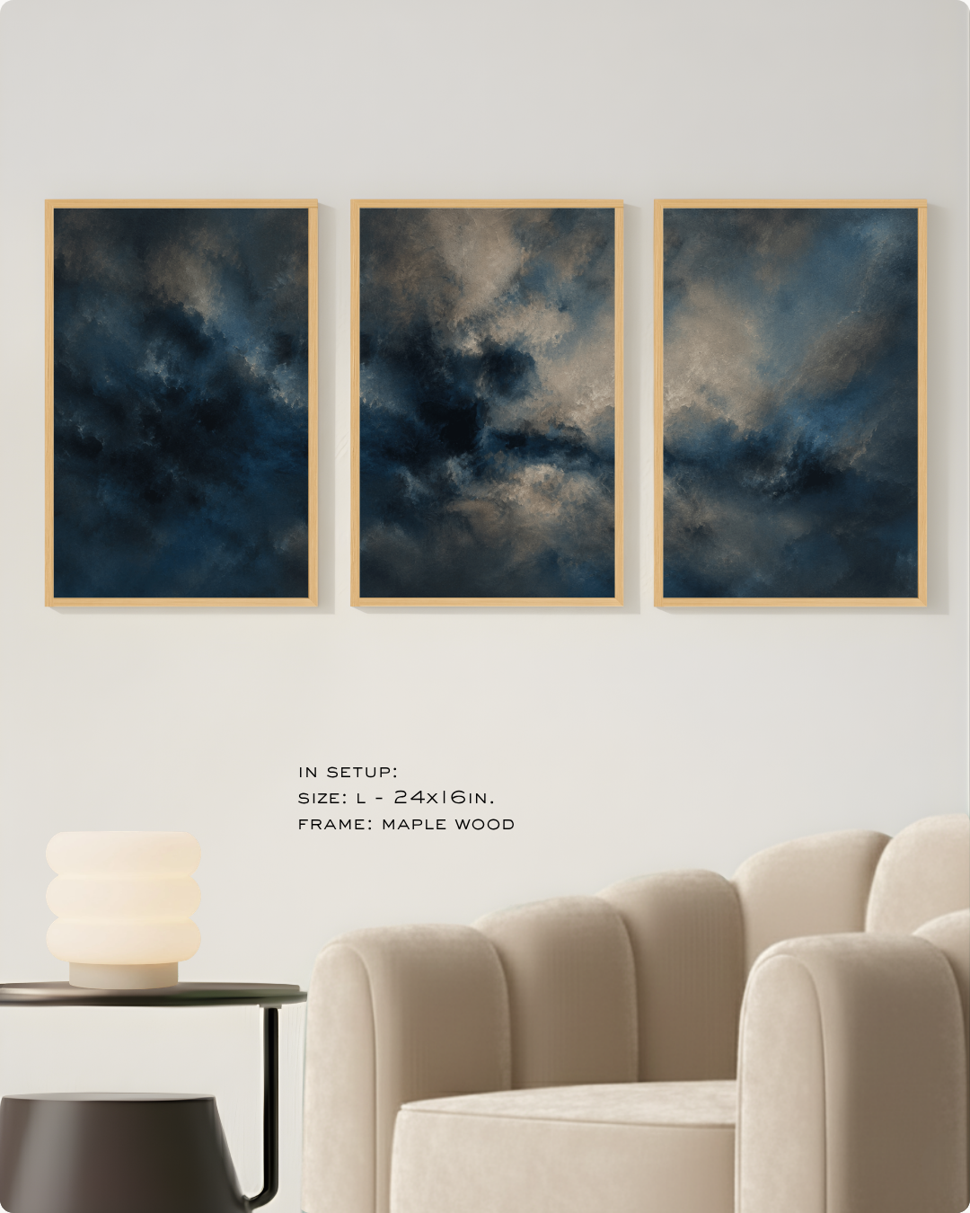 Three framed abstract wall art prints hang side by side on a light wall above a beige armchair, with small text noting the size and maple wood frame. The artwork depicts dark blue, gray, and white storm-like clouds.