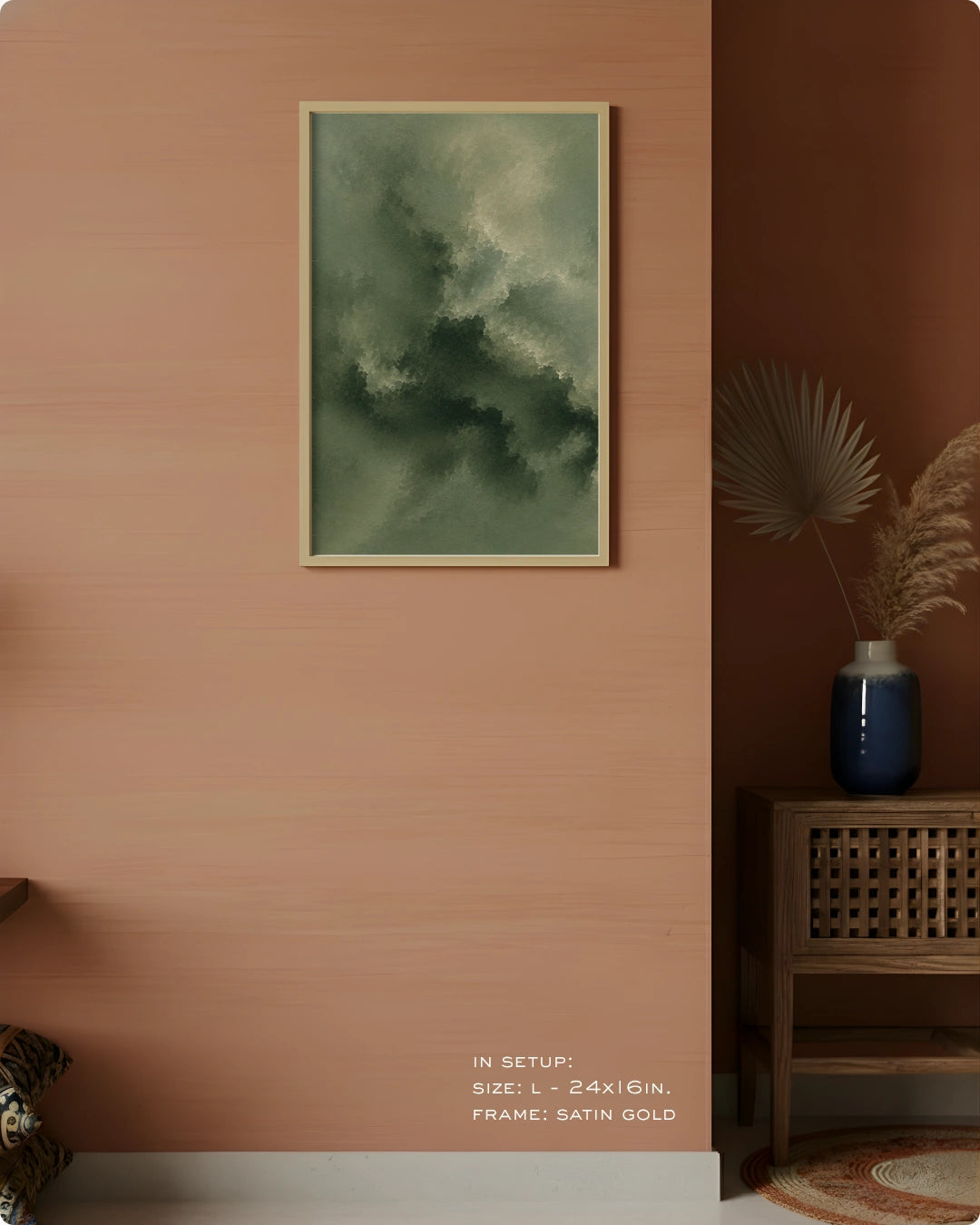 A framed abstract art print featuring a textured green and gray cloud-like pattern in satin gold, displayed on a warm terracotta wall in a styled interior setting.