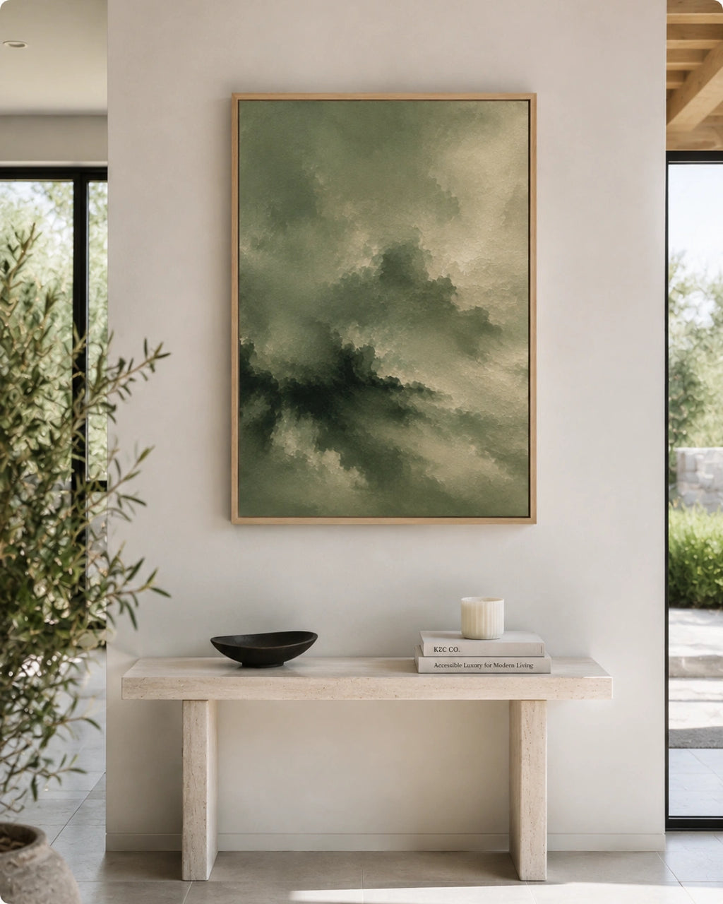 A framed abstract landscape painting in muted green and gray tones hangs on a light beige wall above a minimalist stone console table with a black bowl and books in a modern interior setting.