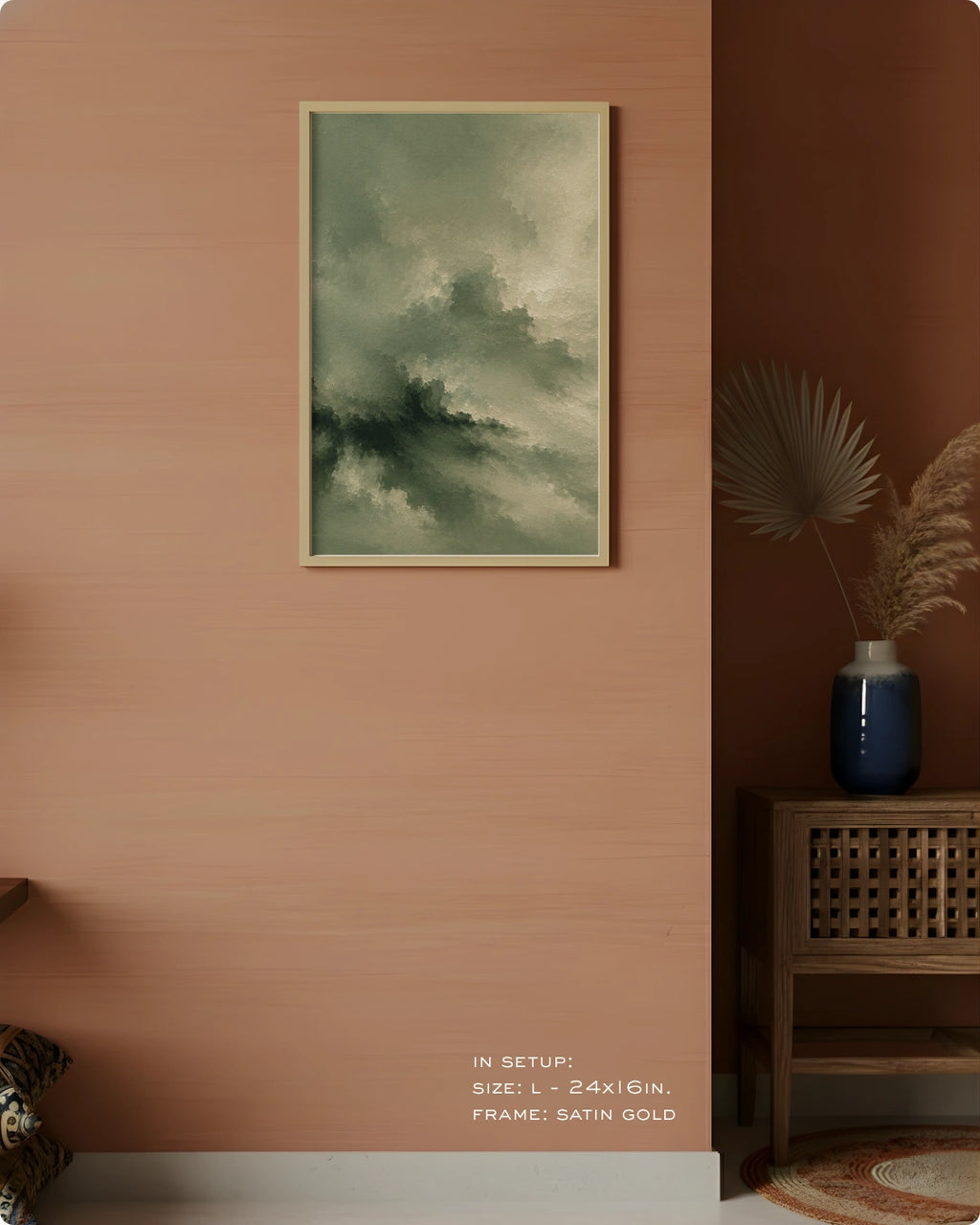 A framed abstract landscape art print featuring green and gray clouds, displayed on a textured terracotta wall in a styled interior setting with a wooden side table and a blue vase.