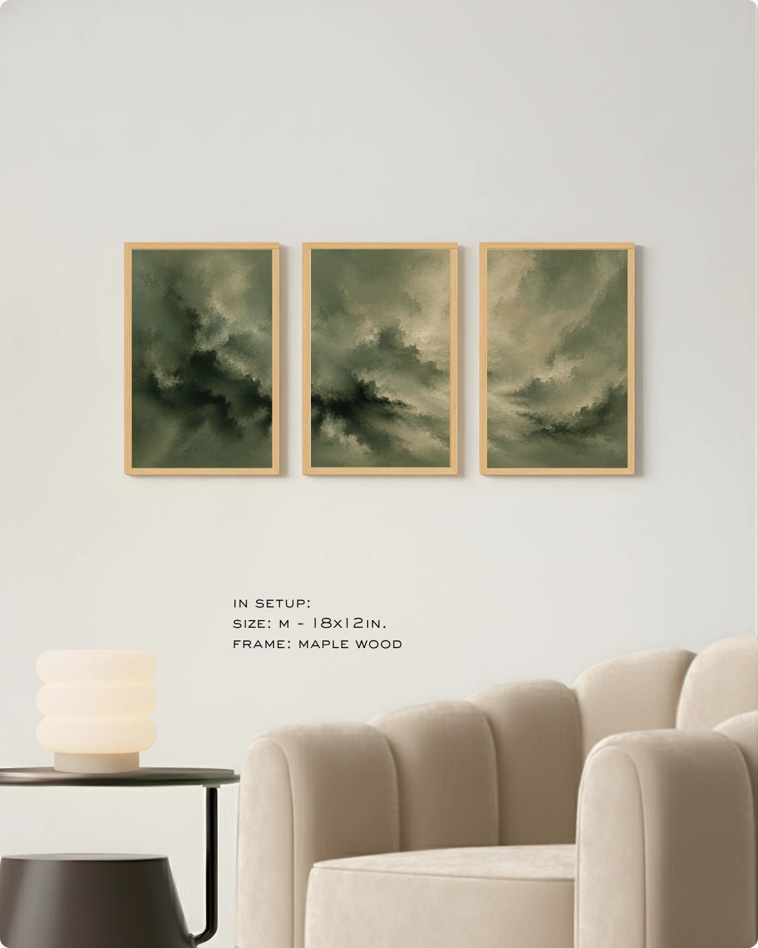 Three framed vertical wall art prints with dark green and gray stormy clouds hang on a light gray wall above a beige armchair. Small text below reads 'IN SETUP: SIZE: M - 18x12 IN.