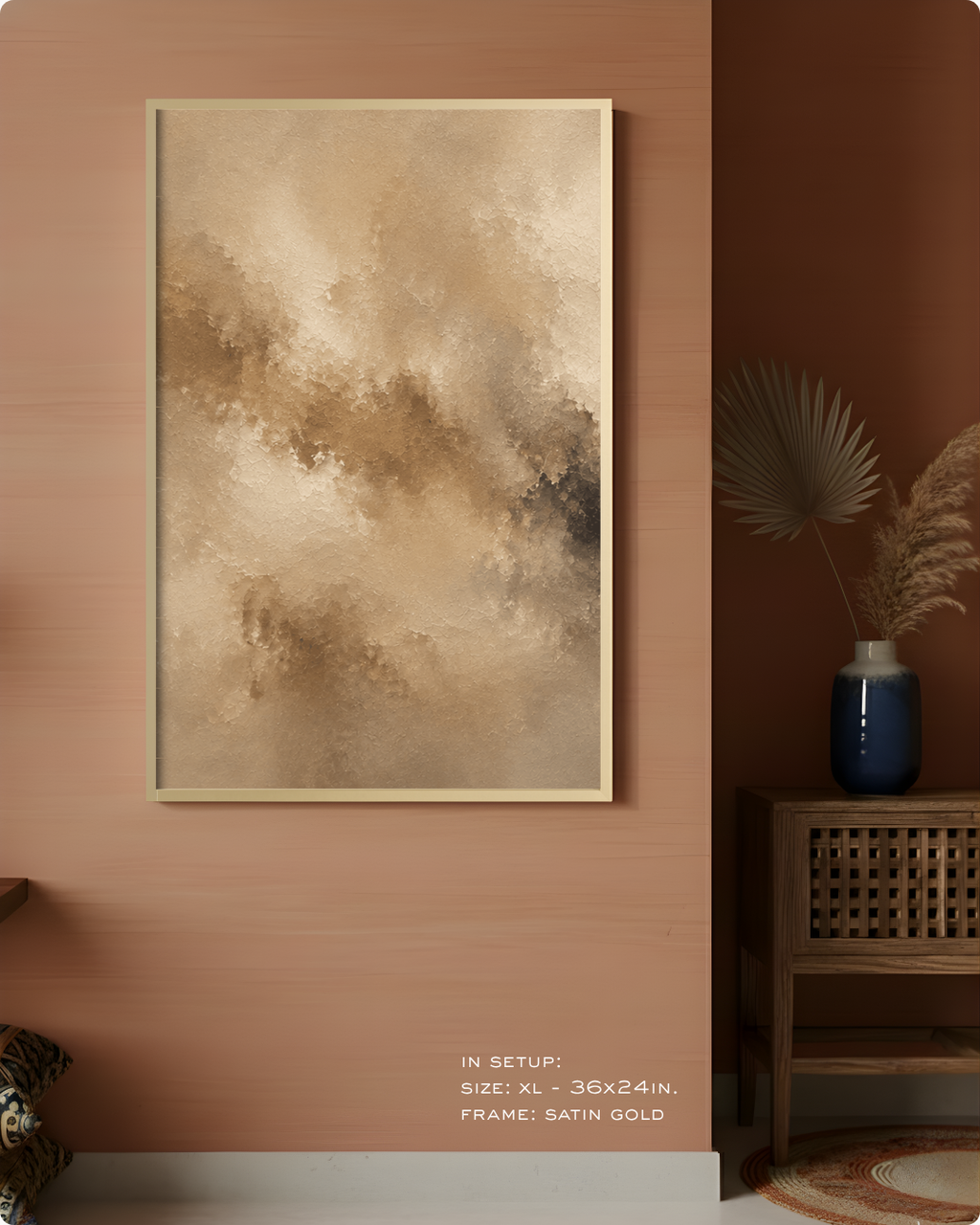 Abstract framed wall art hanging on a warm terracotta wall in a styled interior. The artwork features soft beige, tan, and brown painterly brushstrokes with a thin satin gold frame.
