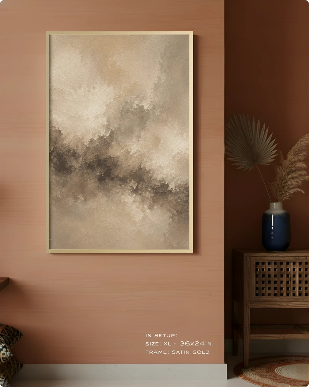 A framed abstract canvas print with textured beige, gray, and brown brushstrokes, displayed on a warm terracotta wall in a styled interior setting with a side table and vase.