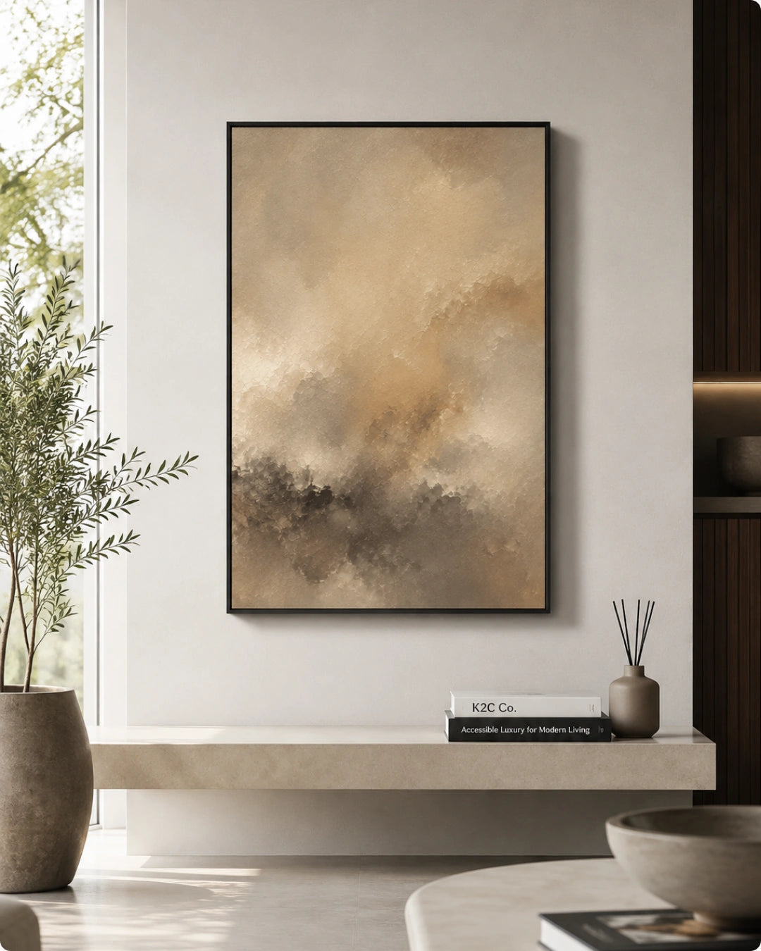 A framed abstract art print with a black frame hangs on a light gray wall in a modern interior setting. The artwork features a textured, painterly design in warm beige, brown, and gray tones.