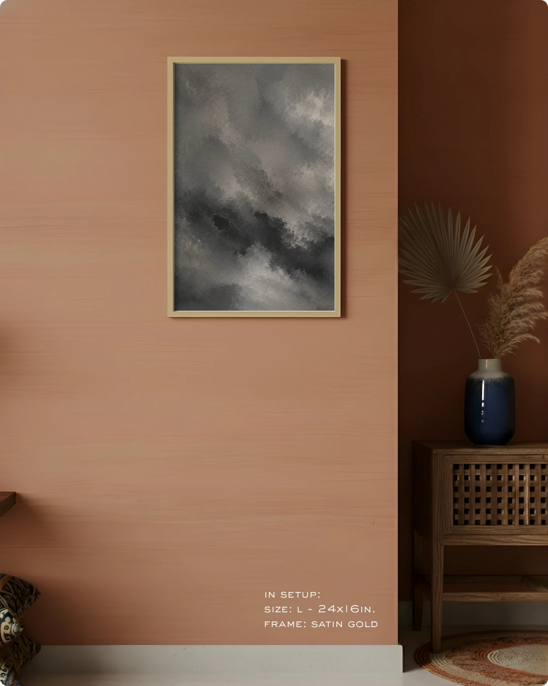 A framed wall art print featuring a dramatic dark gray cloudy sky, styled in a modern interior setting on a warm terracotta wall next to a wooden side table with a blue vase.