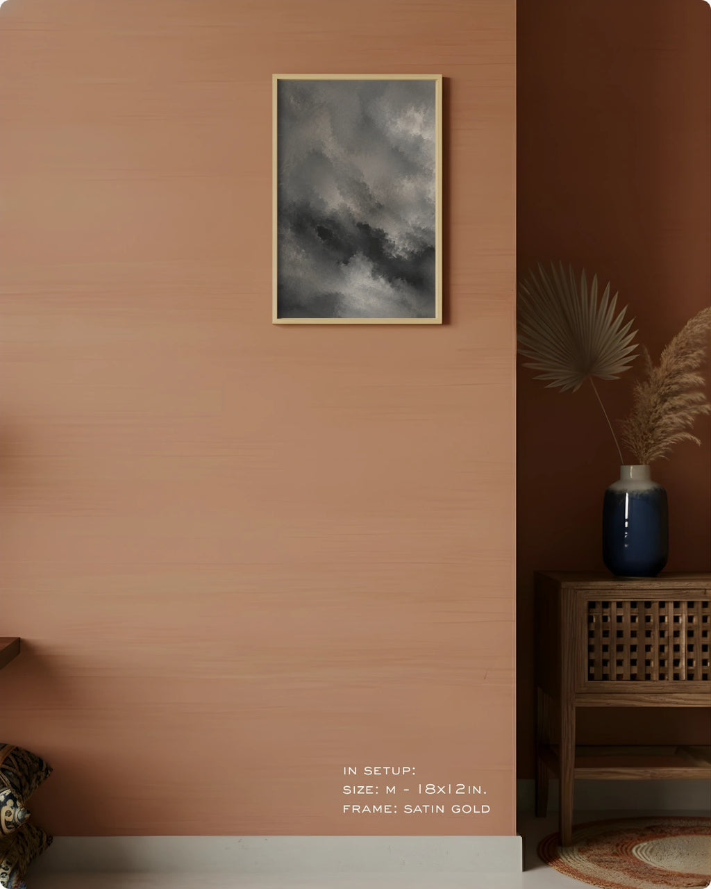 A framed wall art print depicting a dark, moody stormy sky hangs on a warm terracotta-colored wall in a styled interior setting. The frame is satin gold.