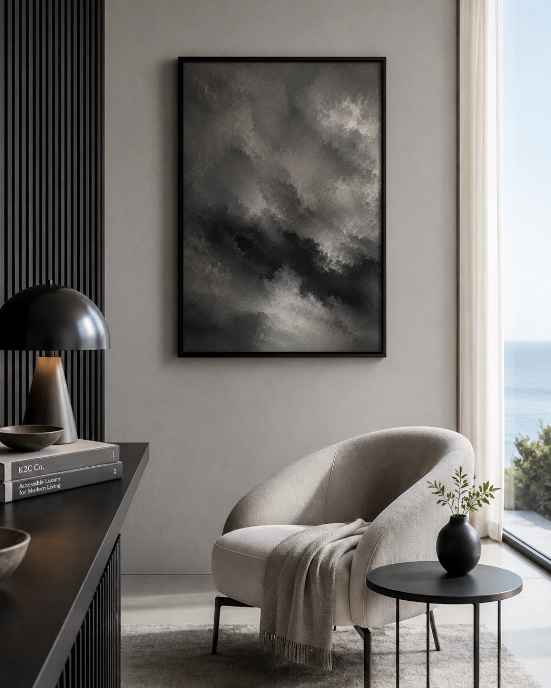 A framed black and white dramatic storm cloud art print hanging on a light gray wall in a modern living room setting with a beige armchair, side table, and window view.