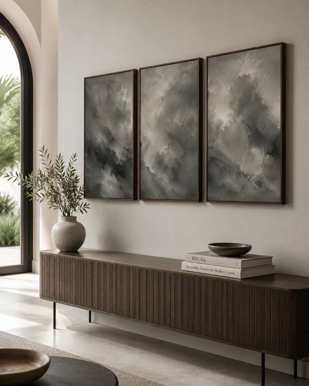 Three framed vertical canvas prints with dark gray and black stormy cloud artwork, displayed on a light beige wall above a long dark wood console table in a modern interior setting.