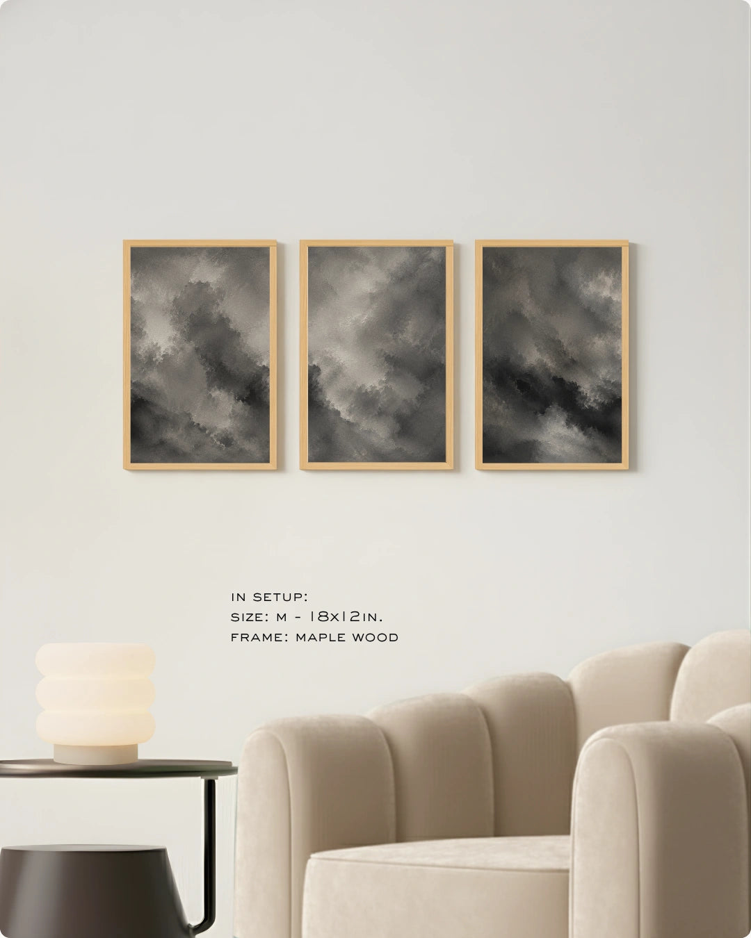 Three vertical framed wall art prints with dark gray cloudy artwork in light wood frames, displayed above a beige armchair in a modern room setting.