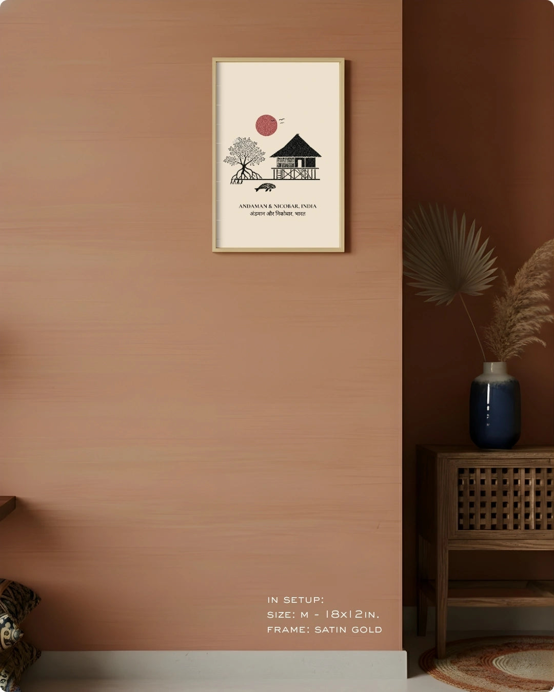 A framed minimalist art print hangs on a warm terracotta-colored wall in a styled interior setting. The print features a black line drawing of a house and tree with a red sun, plus small text.
