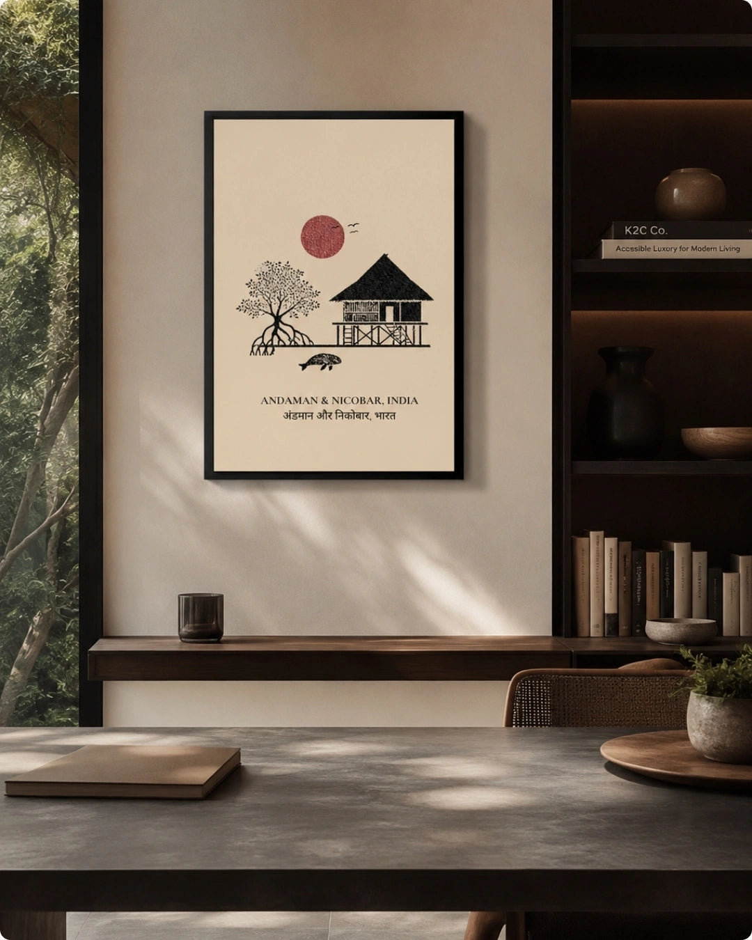 A framed minimalist art print hangs on a beige wall in a modern interior setting. The print features a black line drawing of a house and tree with a red sun and the text 'ANDAMAN & NICOBAR INDIA' below.