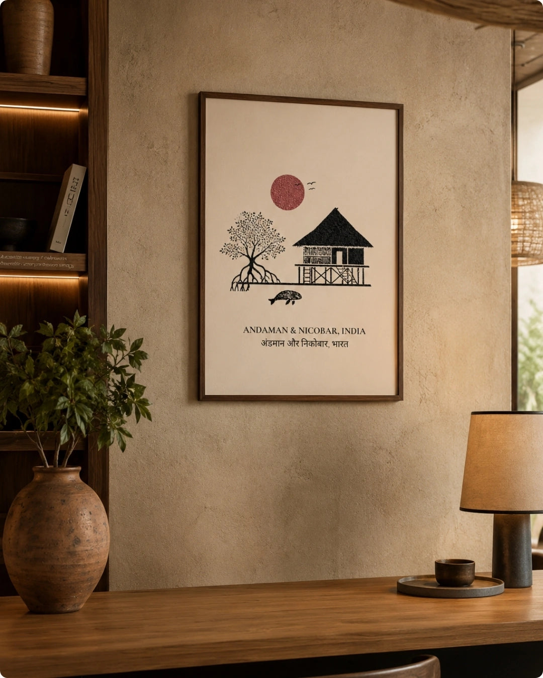 A framed minimalist art print featuring a black line drawing of a house and tree with a muted red sun, hanging on a textured beige wall above a wooden table with a lamp and vase.