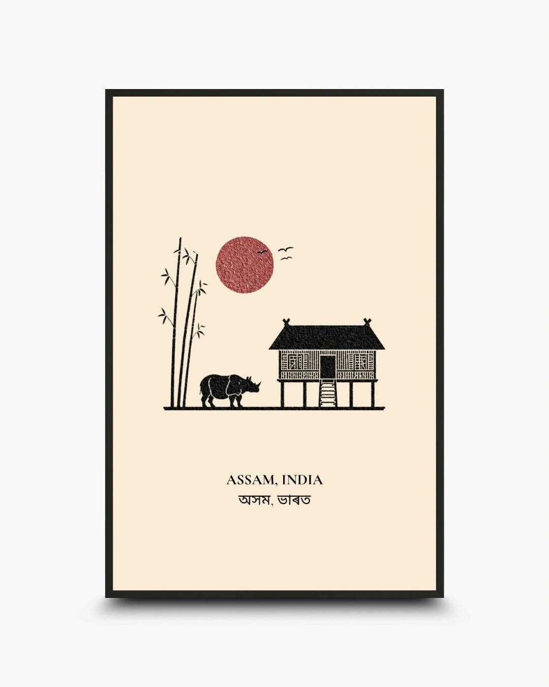 A framed minimalist art print featuring a black stilt house, a rhinoceros, bamboo, birds, and a red sun on a cream background, with the text 'ASSAM, INDIA' and Bengali script below. The print is shown in a black frame against a light gray background.