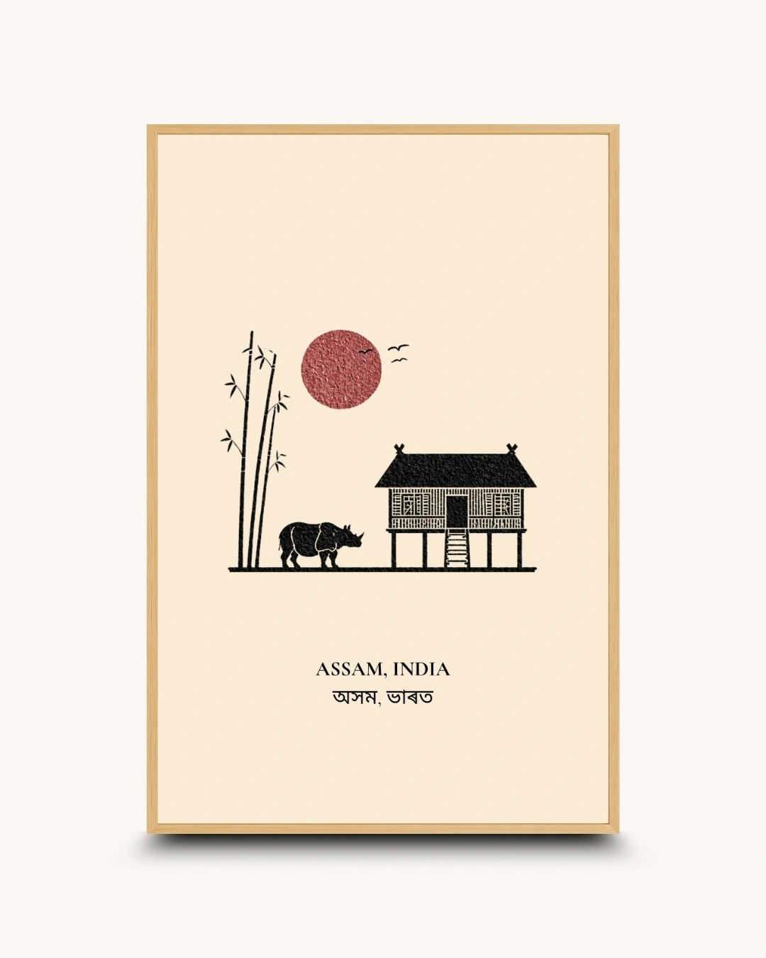 A framed art print featuring a minimalist illustration of Assam, India, with a stilt house, a rhinoceros, bamboo, a red sun, and text reading 'ASSAM, INDIA' and 'हंक नेऒका'. The print has a cream background, a light wood frame, and is shown against a light gray background.