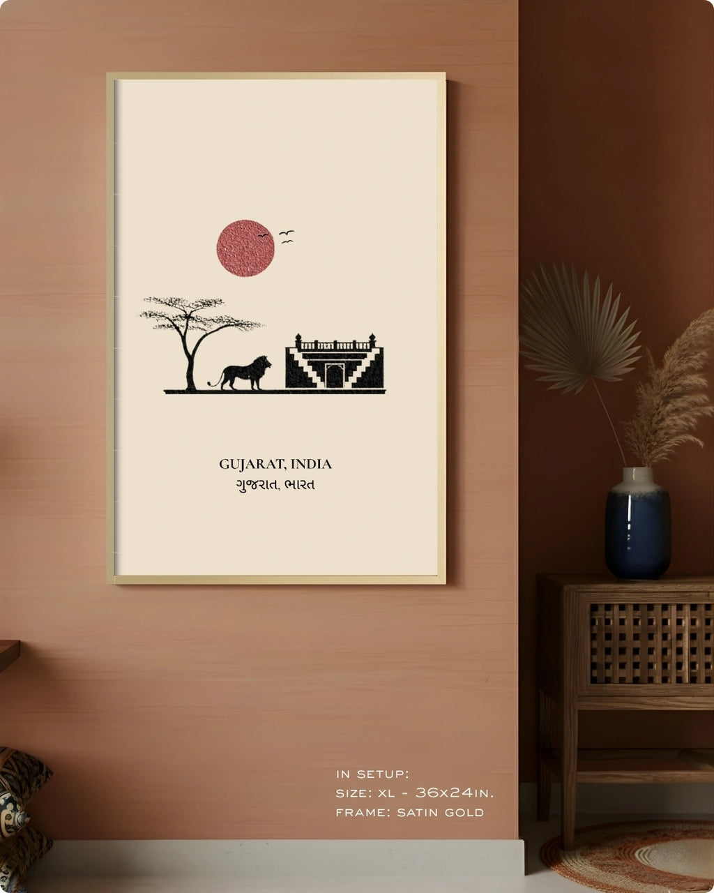 A framed wall art print featuring a minimalist illustration of Gujarat, India, with a red sun, black silhouette of a tree and animal, and a temple, displayed on a warm terracotta wall in a styled interior setting.