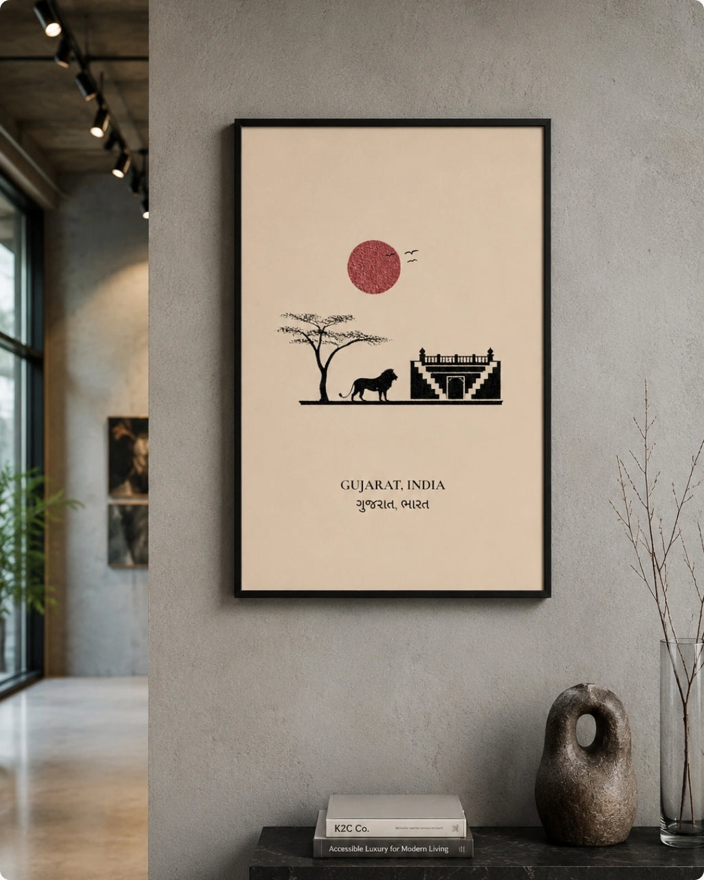 A framed minimalist art print of Gujarat, India, featuring a black silhouette of a lion, acacia tree, and temple against a beige background with a red sun, displayed on a gray wall in a modern interior setting.