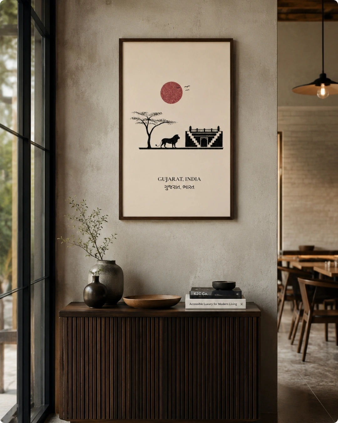 A framed art print featuring a minimalist black and red illustration of a tree, a lion, and a fort, with the text 'GUJARAT, INDIA' and Gujarati script below, displayed on a textured gray wall in a modern interior setting.