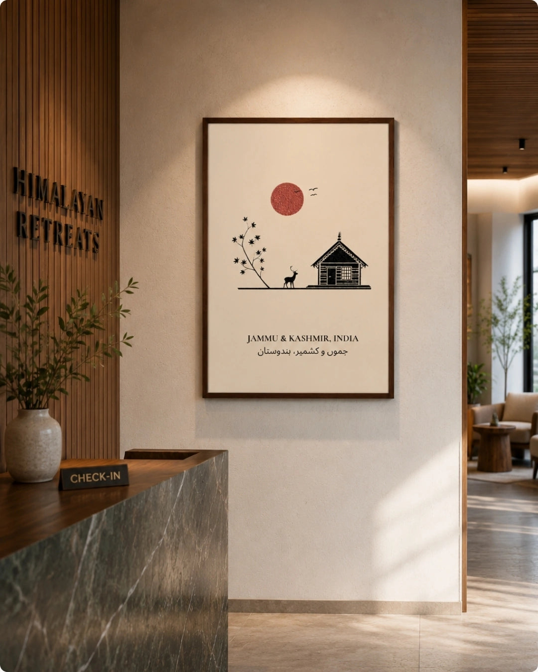 A framed minimalist art print hangs on a beige wall in a modern lobby. The print features a black line drawing of a house, a small dog, and trees with a red sun, and the text 'JAMMU & KASHMIR, INDIA' along with Sindhi script.