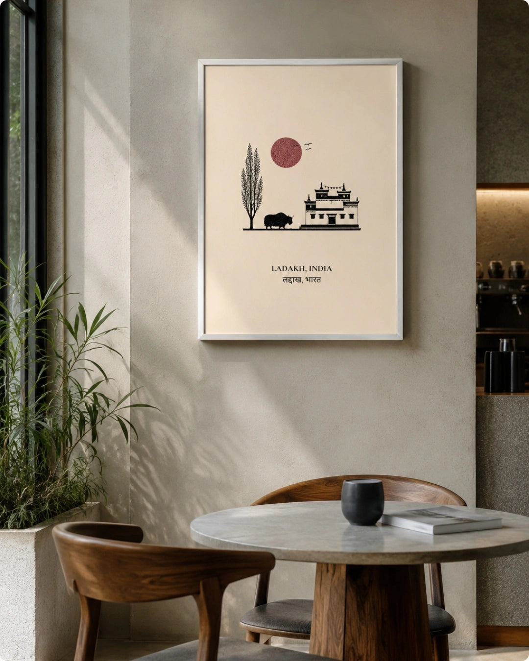 A framed minimalist art print of Ladakh, India, hanging on a beige wall in a modern dining room setting with a wooden table and chairs.