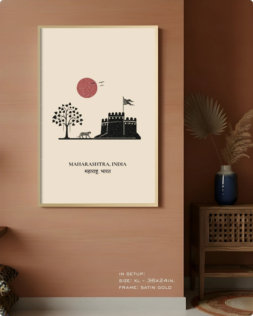 A framed wall art print hangs on a warm terracotta wall in a styled interior. The print shows a minimalist black illustration of a castle and tree with a pink-red sun, plus the text 'MAHARASHTRA, INDIA' and Devanagari text below.