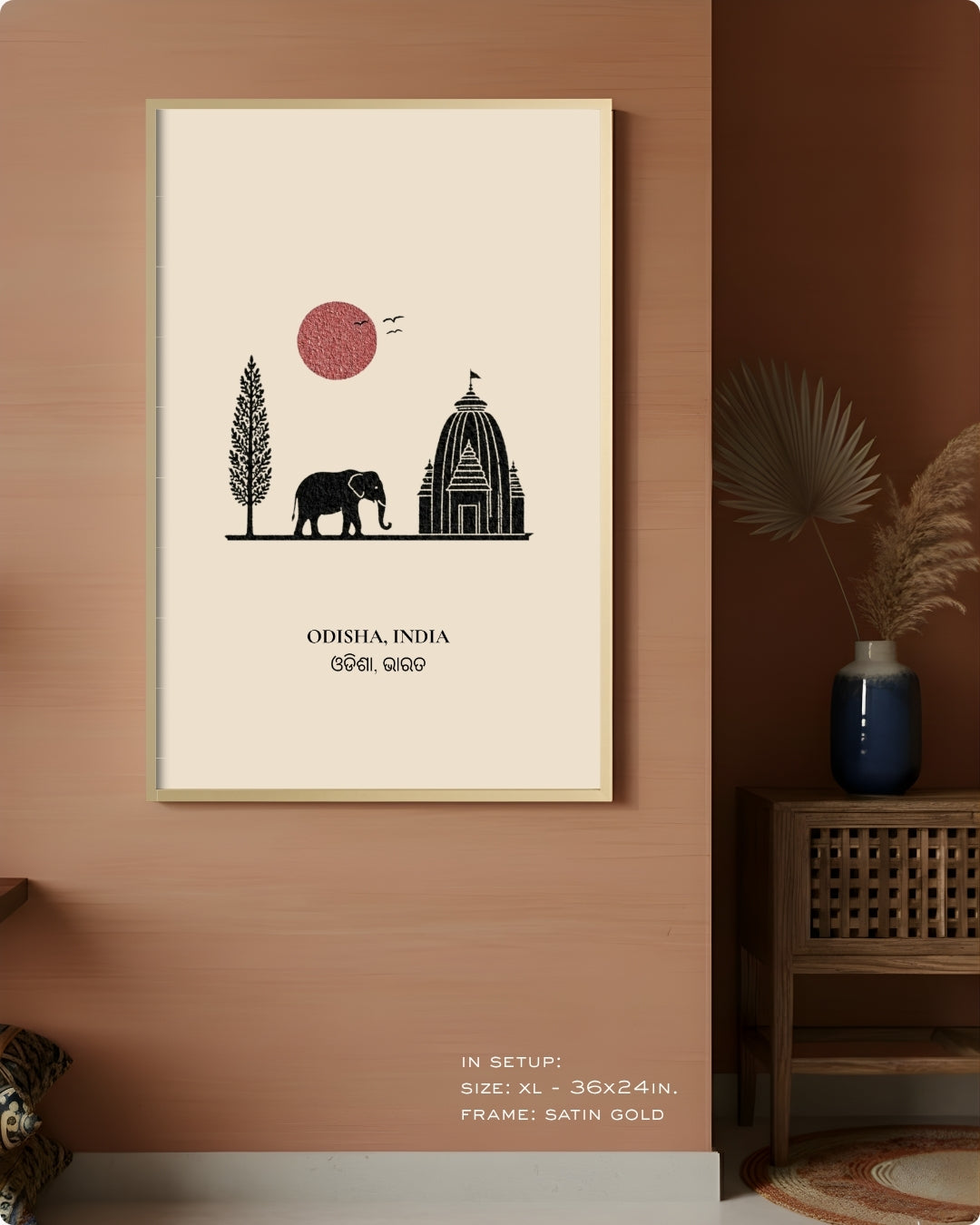 A framed art print featuring a minimalist black line drawing of an elephant, a temple, a tree, and a pink sun on an off-white background, hanging on a terracotta-colored wall in a styled interior setting.