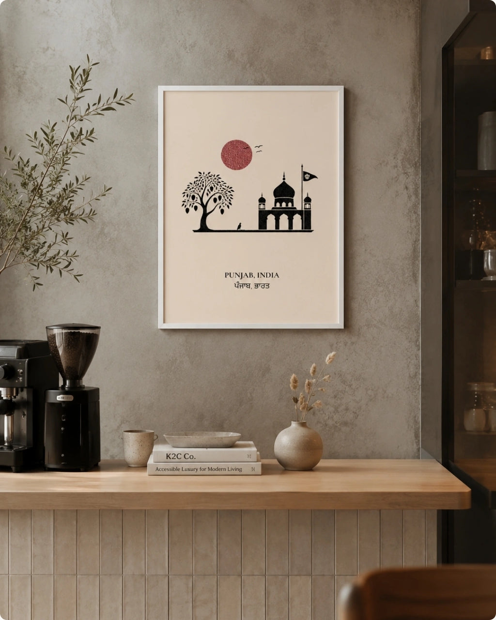 A framed minimalist art print featuring a black silhouette illustration of a mosque and tree with a red sun on a cream background, hanging on a textured gray wall above a wooden counter in a styled interior setting.
