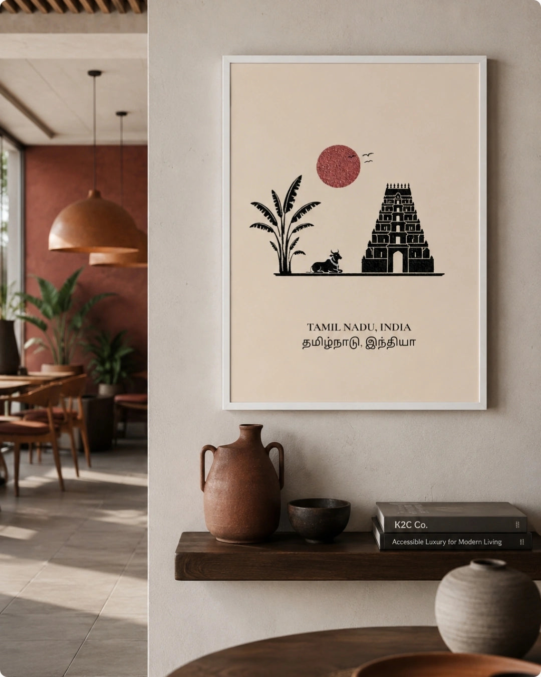 A framed minimalist Tamil Nadu India art print with a black temple, plant, and red sun on a cream background, hanging on a wall in a modern interior setting.