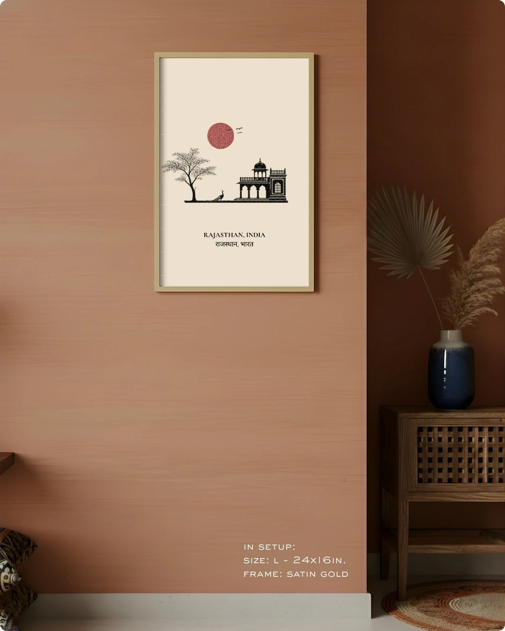 A framed vertical art print featuring a minimalist black line drawing of a monument and tree with a red sun on an off-white background, hung on a warm peach wall in a styled interior setting.