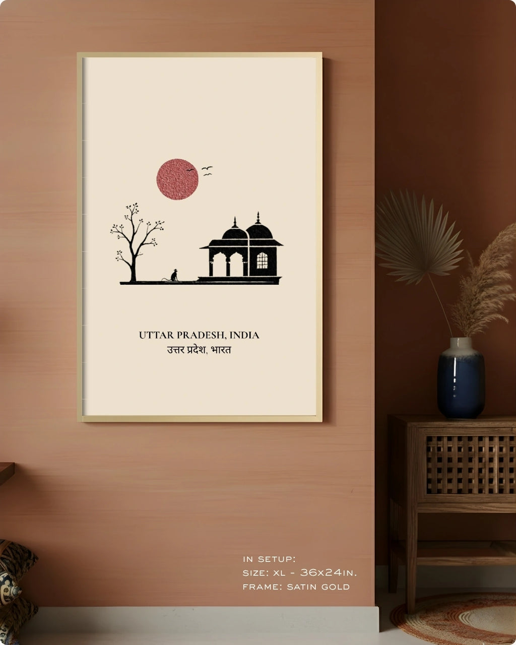 A framed wall art print featuring a minimalist black illustration of a domed building and tree under a pink sun on an off-white background, hung on a terracotta-colored wall in a styled interior setting.
