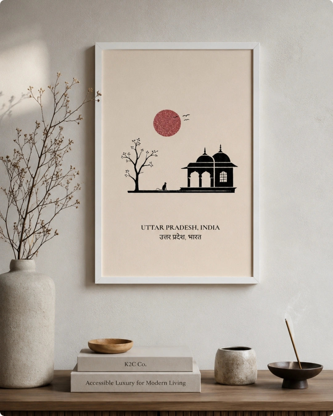 A framed minimalist art print of Uttar Pradesh, India, featuring a black silhouette of a domed palace and tree against a beige background with a red sun, styled on a wall above a wooden shelf with books and decorative items.