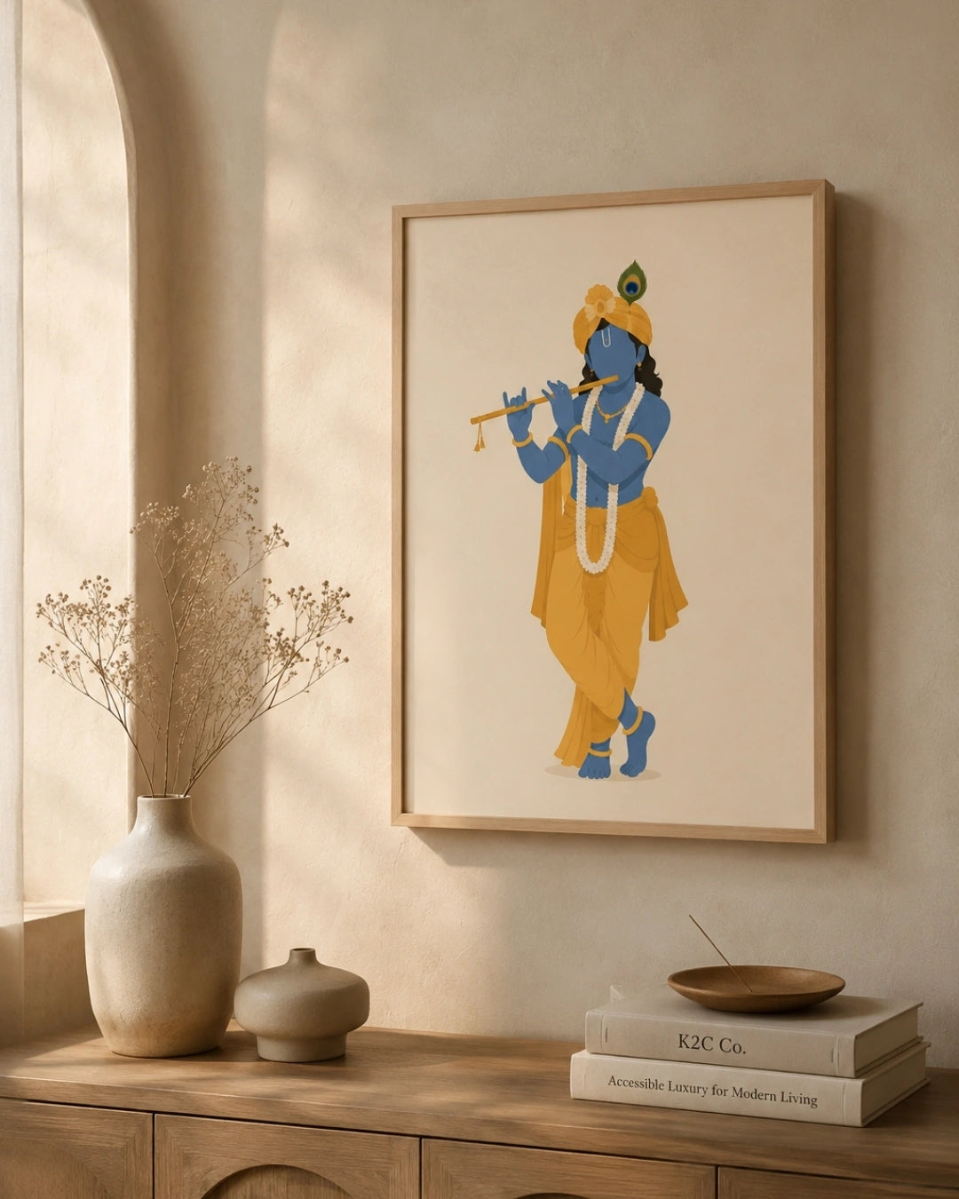 A framed art print of ISKCON Krishna playing a flute, styled on a beige wall above a wooden console table with a vase and books.