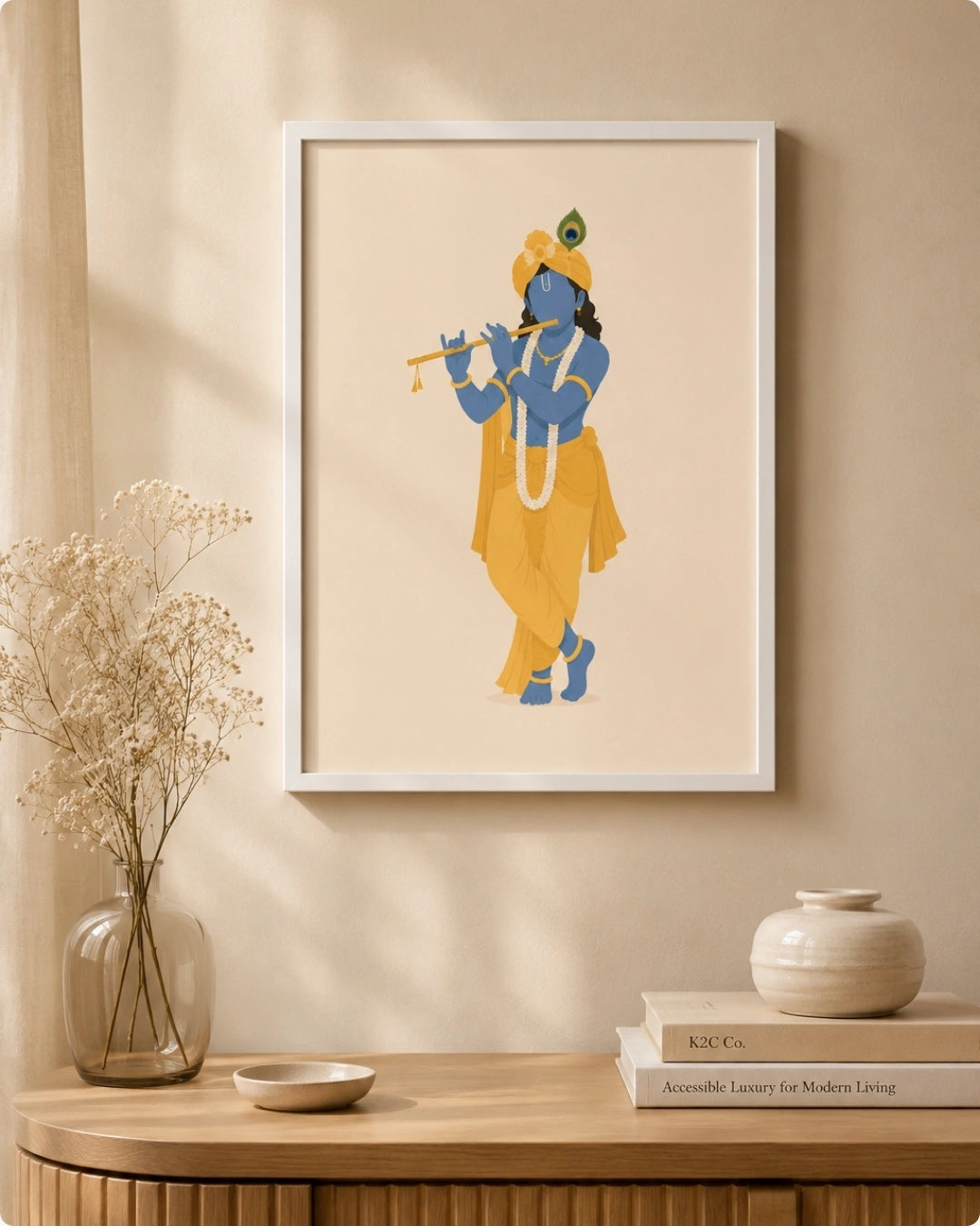 A framed art print featuring a stylized illustration of ISKCON Krishna playing a golden flute, hung on a beige wall above a wooden console table with a vase of dried flowers and decorative objects.