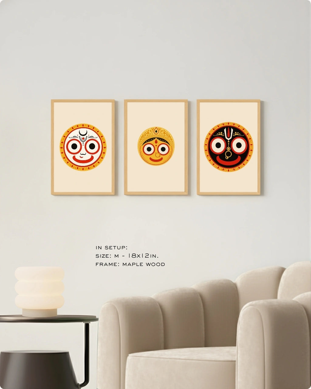 Visual size guide mockup for the Jagannath Triad 3-piece wall art set in Medium size with satin gold frames, displayed above a modern ribbed beige armchair.