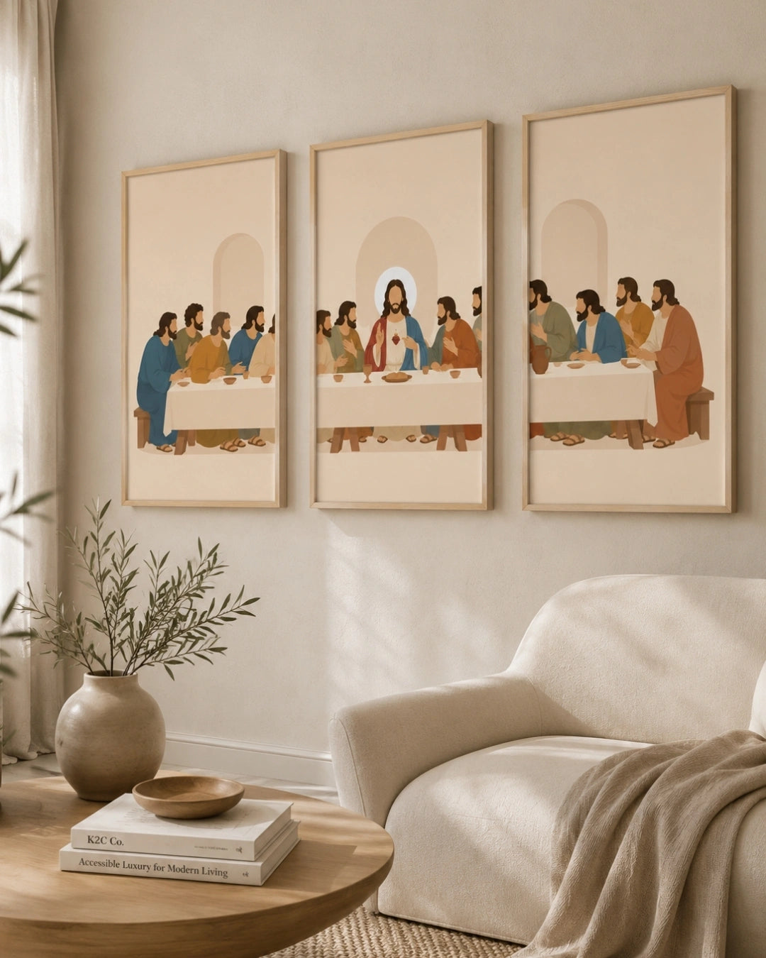 Three framed art prints depicting a stylized version of the Last Supper hang on a beige wall above a cream armchair and a round wooden coffee table with a vase and books.